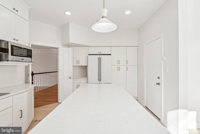 kitchen with hanging light fixtures, high end fridge, white cabinets, and light wood-type flooring