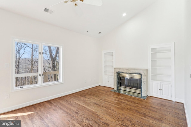 unfurnished living room featuring built in features, a high end fireplace, high vaulted ceiling, and wood-type flooring