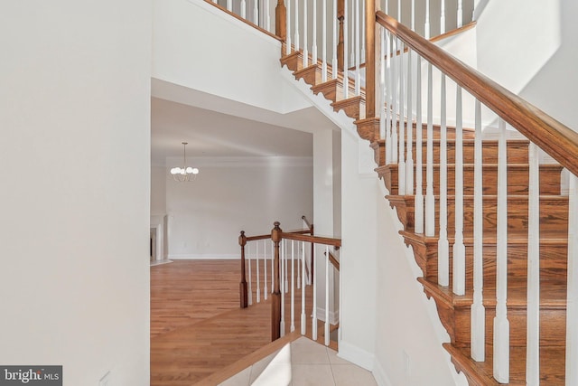 staircase featuring an inviting chandelier, hardwood / wood-style flooring, ornamental molding, and a high ceiling