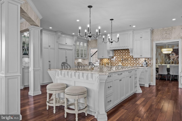 kitchen with a breakfast bar, decorative light fixtures, paneled fridge, white cabinets, and a kitchen island with sink