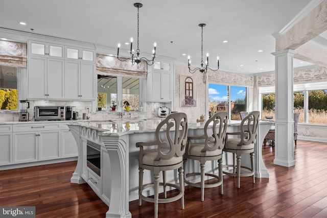 kitchen featuring a kitchen island, light stone countertops, ornate columns, white cabinets, and pendant lighting