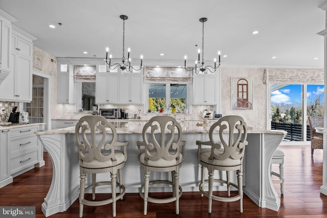 kitchen featuring a kitchen island, white cabinets, light stone counters, and decorative light fixtures