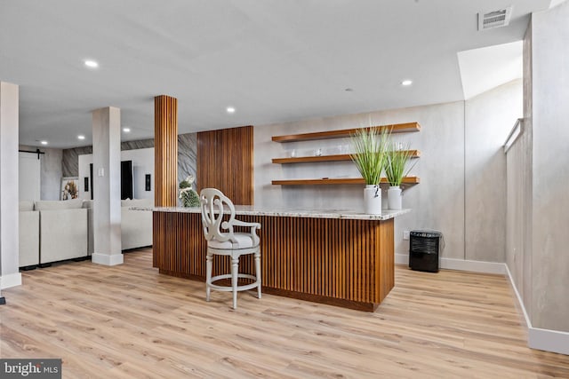 kitchen with a barn door, kitchen peninsula, a kitchen bar, and light hardwood / wood-style flooring