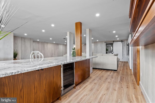 kitchen with wine cooler, light wood-type flooring, a barn door, and light stone counters