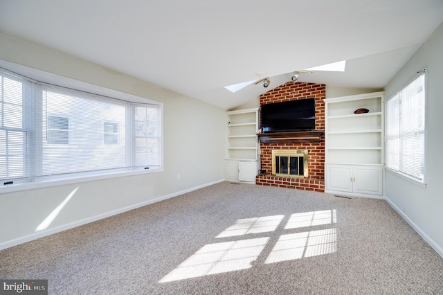 unfurnished living room with carpet floors, plenty of natural light, a fireplace, and vaulted ceiling with skylight