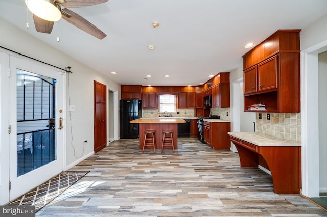 kitchen with a breakfast bar, black appliances, a center island, light hardwood / wood-style flooring, and backsplash