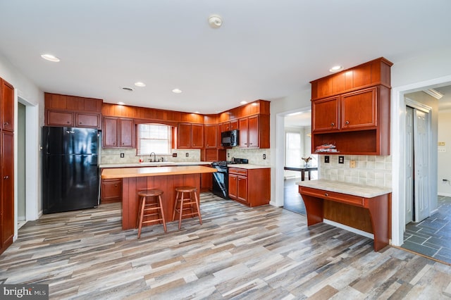 kitchen with backsplash, black appliances, a breakfast bar, and a kitchen island