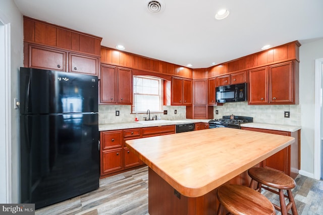 kitchen featuring sink, a center island, light hardwood / wood-style floors, decorative backsplash, and black appliances