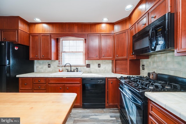 kitchen featuring sink, decorative backsplash, light wood-type flooring, and black appliances