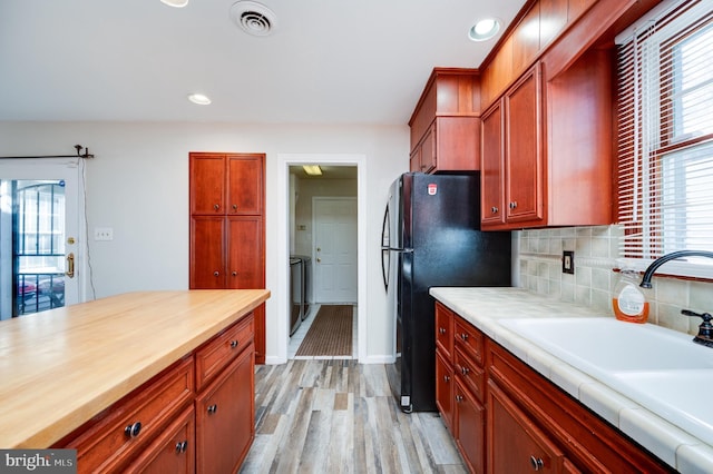 kitchen with tasteful backsplash, sink, black refrigerator, and light wood-type flooring