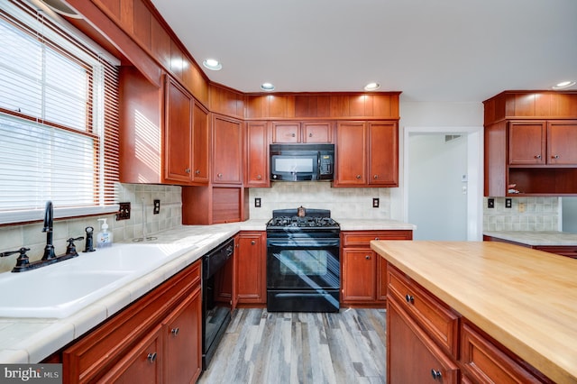 kitchen with tasteful backsplash, sink, black appliances, and light wood-type flooring