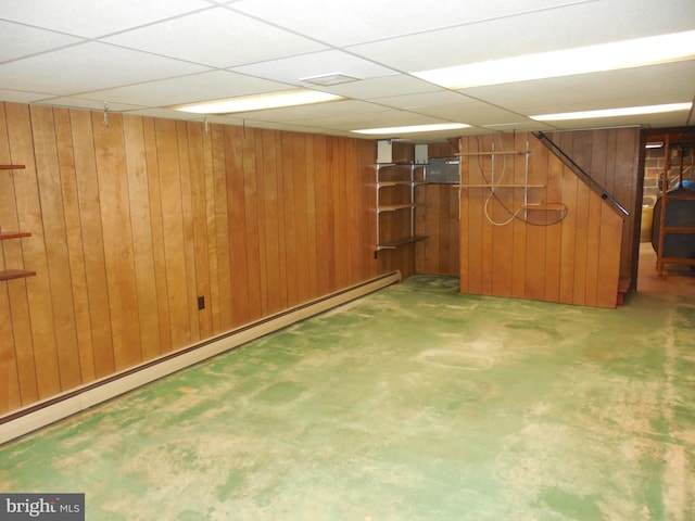 basement with wooden walls, a drop ceiling, and baseboard heating