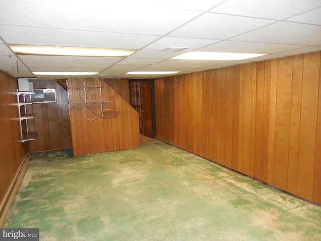 basement featuring a drop ceiling, wooden walls, and baseboard heating