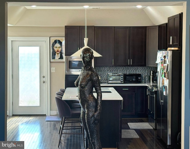 kitchen with a kitchen bar, a center island, appliances with stainless steel finishes, dark hardwood / wood-style floors, and decorative backsplash