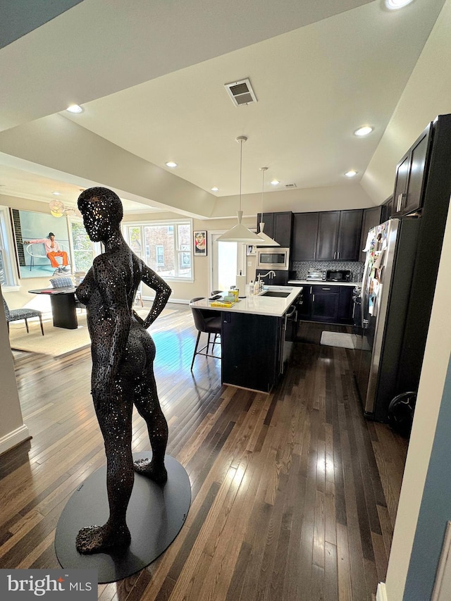 kitchen with pendant lighting, appliances with stainless steel finishes, a kitchen island with sink, tasteful backsplash, and dark hardwood / wood-style flooring