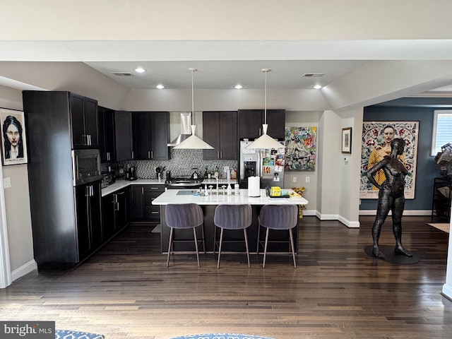 kitchen featuring decorative light fixtures, a kitchen bar, a center island, stainless steel appliances, and wall chimney range hood