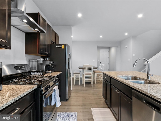 kitchen with sink, light hardwood / wood-style flooring, stainless steel appliances, light stone counters, and wall chimney exhaust hood