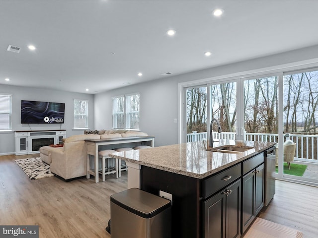 kitchen featuring sink, a center island with sink, light hardwood / wood-style flooring, stainless steel dishwasher, and light stone countertops