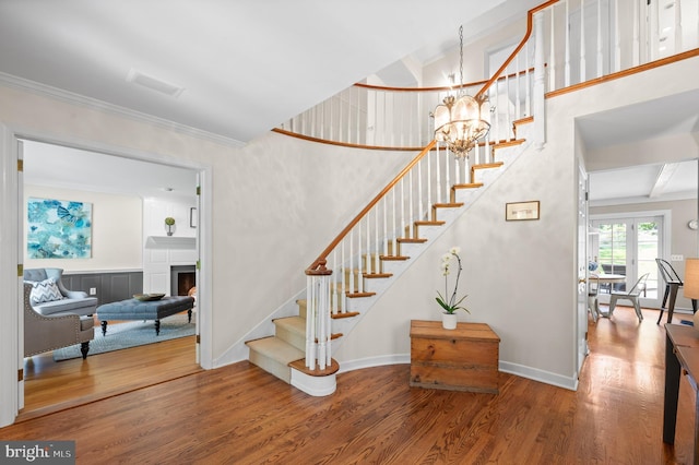 stairs with wood-type flooring, an inviting chandelier, and crown molding