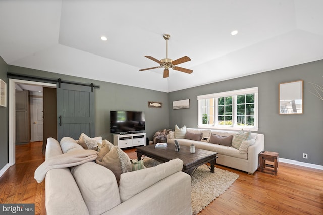 living room featuring ceiling fan, a barn door, a raised ceiling, and light hardwood / wood-style floors