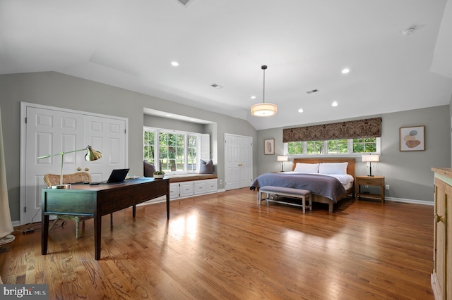 bedroom with vaulted ceiling, light hardwood / wood-style flooring, and two closets