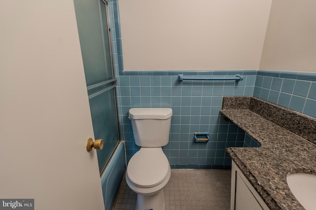 full bathroom with tile walls, bath / shower combo with glass door, vanity, tile patterned floors, and toilet