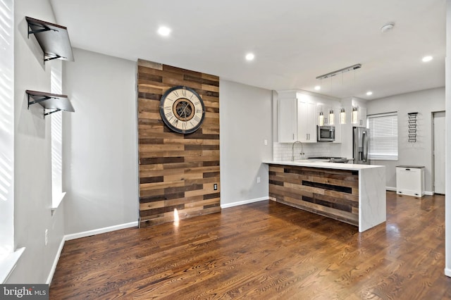 kitchen featuring dark wood-type flooring, light countertops, decorative backsplash, appliances with stainless steel finishes, and a peninsula