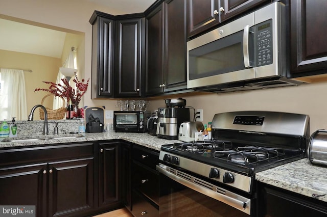 kitchen featuring dark brown cabinetry, sink, light stone counters, and stainless steel appliances