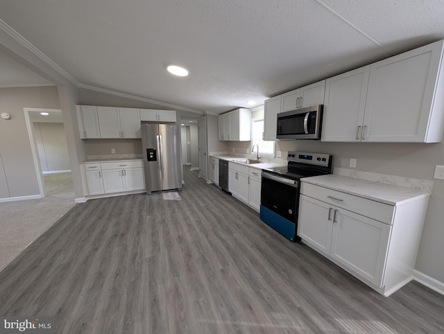 kitchen with stainless steel appliances, vaulted ceiling, sink, and white cabinets