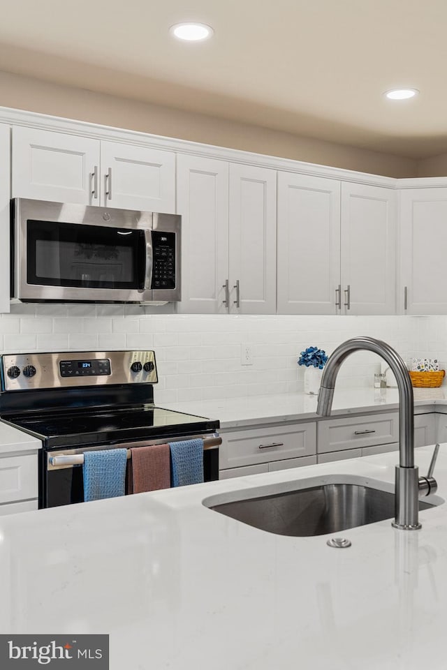 kitchen featuring sink, white cabinets, stainless steel appliances, light stone countertops, and backsplash