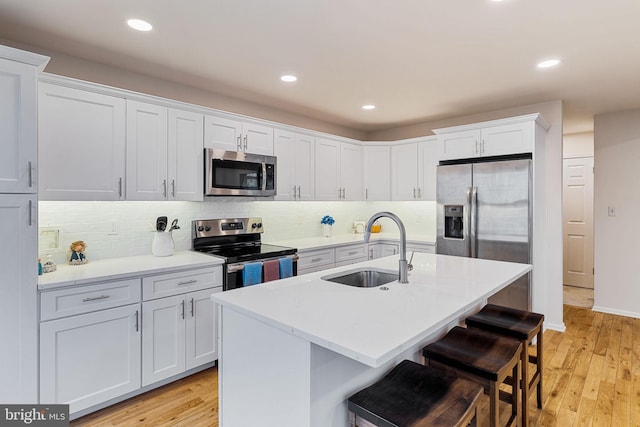 kitchen featuring sink, a breakfast bar area, an island with sink, stainless steel appliances, and white cabinets