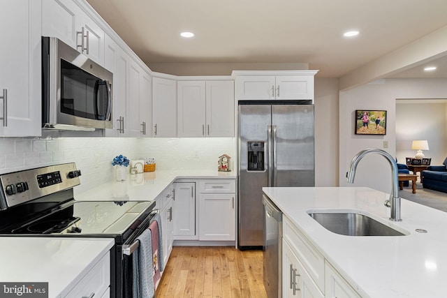 kitchen featuring sink, light hardwood / wood-style flooring, white cabinetry, backsplash, and stainless steel appliances