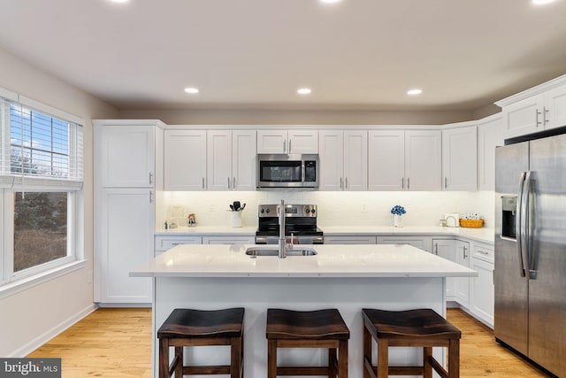 kitchen featuring stainless steel appliances, an island with sink, a kitchen bar, and white cabinetry