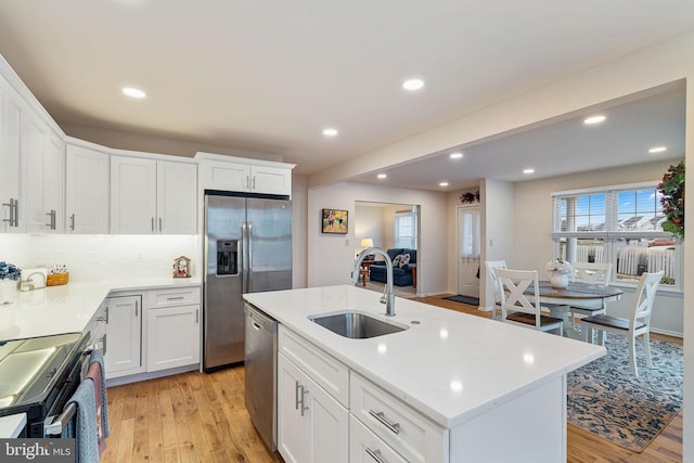 kitchen with sink, white cabinetry, light wood-type flooring, an island with sink, and stainless steel appliances