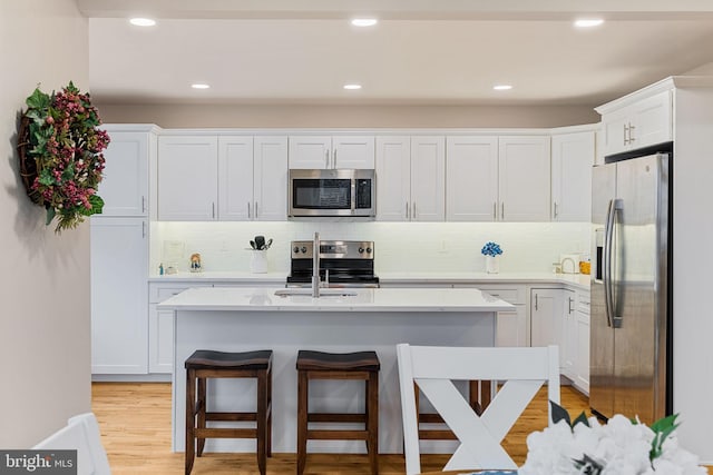 kitchen with light hardwood / wood-style flooring, a breakfast bar, appliances with stainless steel finishes, white cabinetry, and tasteful backsplash