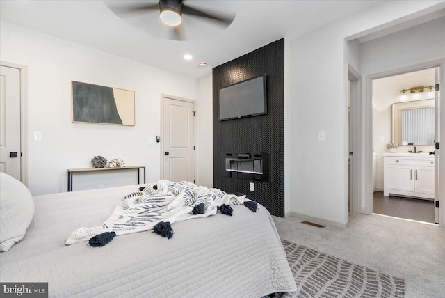 bedroom with sink, ensuite bath, ceiling fan, carpet flooring, and a large fireplace