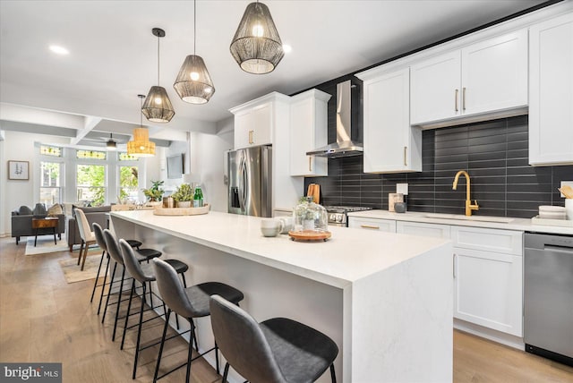 kitchen with white cabinetry, sink, hanging light fixtures, stainless steel appliances, and wall chimney range hood