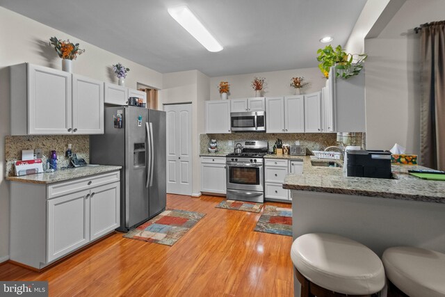 kitchen with appliances with stainless steel finishes, tasteful backsplash, white cabinets, light stone counters, and kitchen peninsula