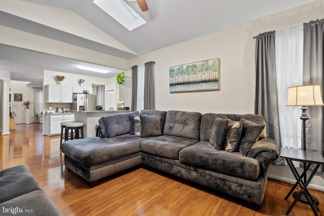 living room with decorative columns, lofted ceiling with skylight, and light hardwood / wood-style flooring