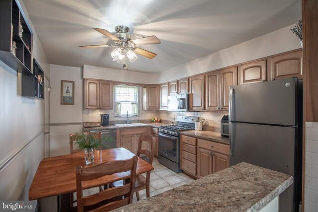 kitchen with sink, decorative backsplash, ceiling fan, light stone counters, and stainless steel appliances