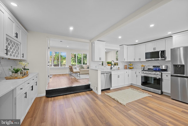 kitchen with appliances with stainless steel finishes, tasteful backsplash, light stone countertops, white cabinets, and light wood-type flooring