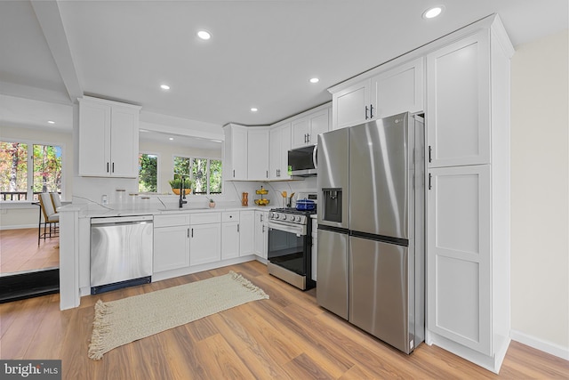 kitchen with sink, appliances with stainless steel finishes, light stone countertops, light hardwood / wood-style floors, and white cabinets