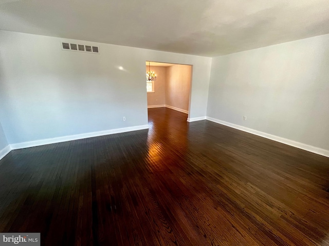 unfurnished room featuring dark wood-type flooring and a notable chandelier