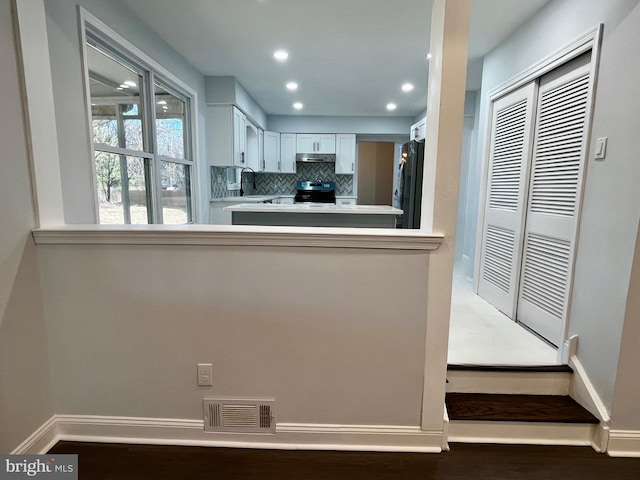 kitchen featuring stainless steel range with electric stovetop, white cabinets, black fridge, decorative backsplash, and kitchen peninsula