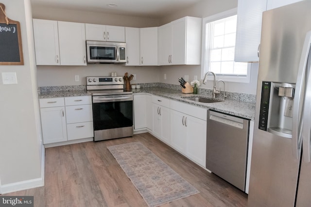 kitchen with sink, light hardwood / wood-style flooring, white cabinetry, stainless steel appliances, and light stone counters