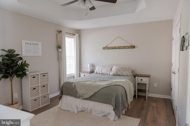 bedroom with dark wood-type flooring, a raised ceiling, and ceiling fan