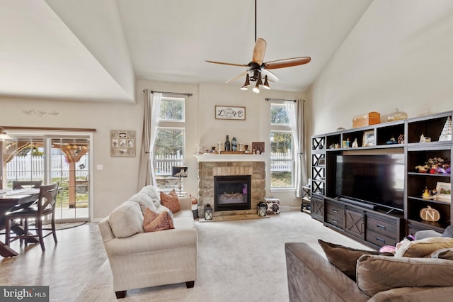 carpeted living room with ceiling fan, a stone fireplace, and high vaulted ceiling