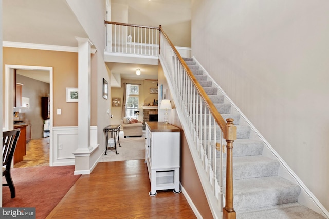 staircase featuring a tile fireplace, decorative columns, hardwood / wood-style flooring, a high ceiling, and crown molding