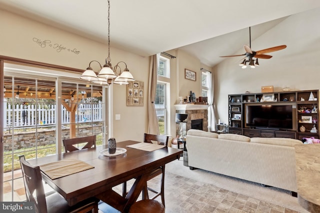 dining room featuring lofted ceiling, a stone fireplace, and ceiling fan with notable chandelier