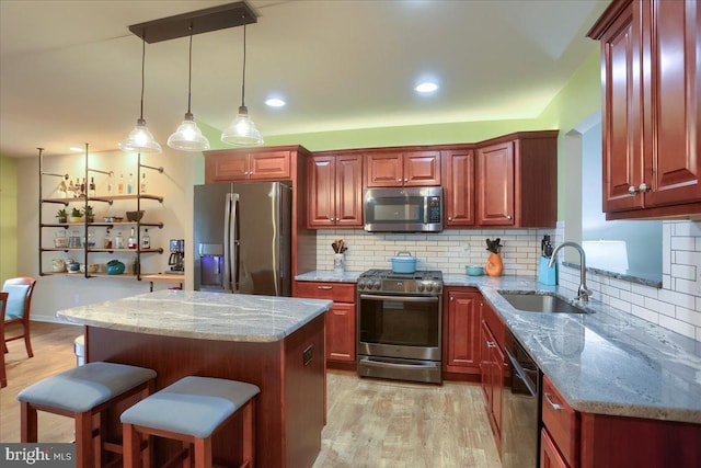 kitchen featuring a kitchen island, appliances with stainless steel finishes, sink, hanging light fixtures, and light stone counters